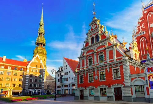 The House of the Blackheads and St. Peter's Church spire in the historic Old Town of Riga, Latvia, with colorful facades and a clear blue sky.