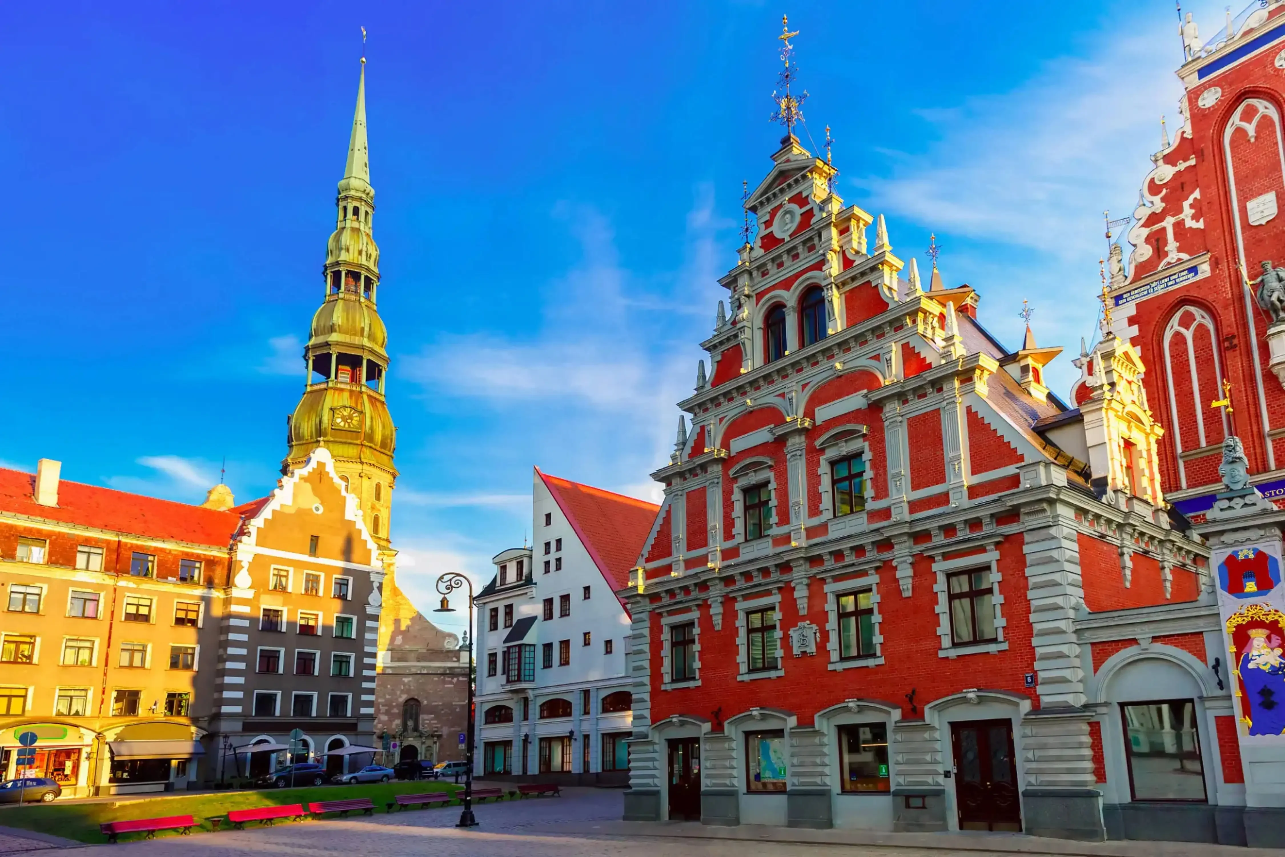 The House of the Blackheads and St. Peter's Church spire in the historic Old Town of Riga, Latvia, with colorful facades and a clear blue sky.