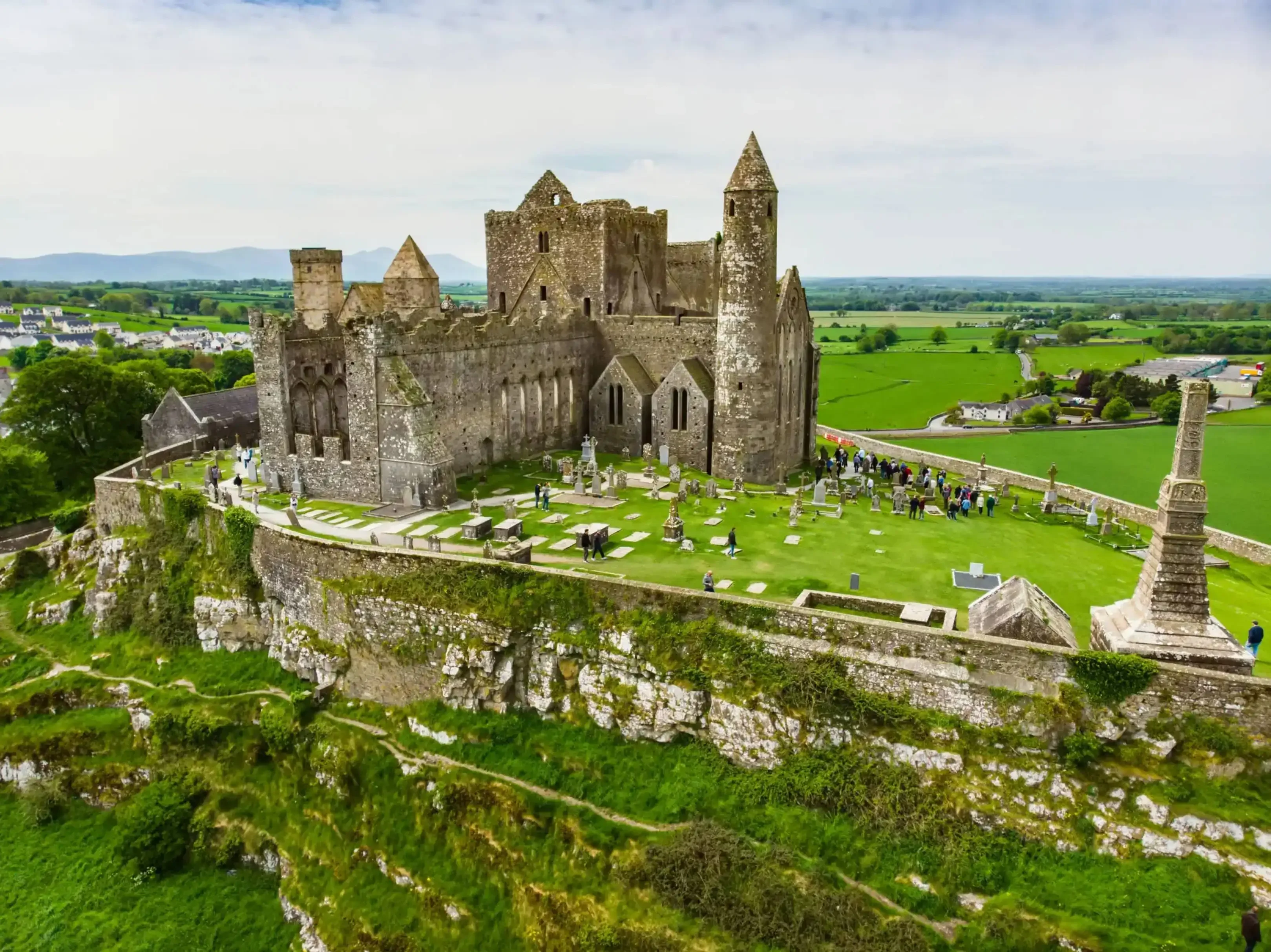 Aerial view of the Rock of Cashel, a historic medieval castle and cathedral ruins atop a green hill in the Irish countryside.