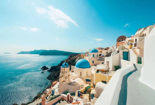 Iconic whitewashed buildings with blue domes overlooking the Aegean Sea in Oia, Santorini, Greece, on a bright sunny day.