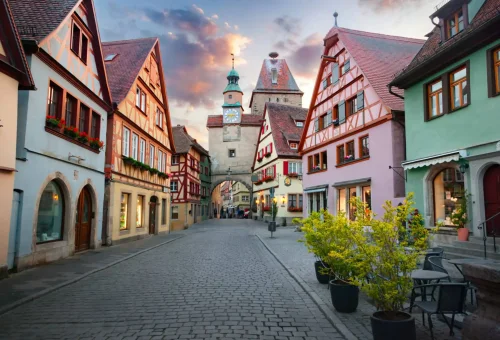 Picturesque medieval street with colorful half-timbered houses leading to a clock tower in Rothenburg ob der Tauber, Germany, under a dramatic evening sky.