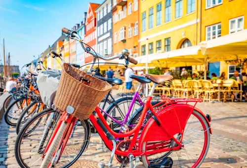 Row of colorful bicycles parked along the cobblestone harborfront of Nyhavn in Copenhagen, Denmark, with vibrant historic buildings and outdoor cafes in the background.