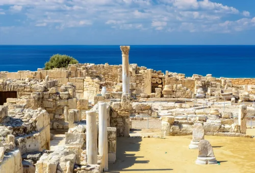 Ancient stone ruins of a Greco-Roman site overlooking the Mediterranean Sea under a partly cloudy sky.