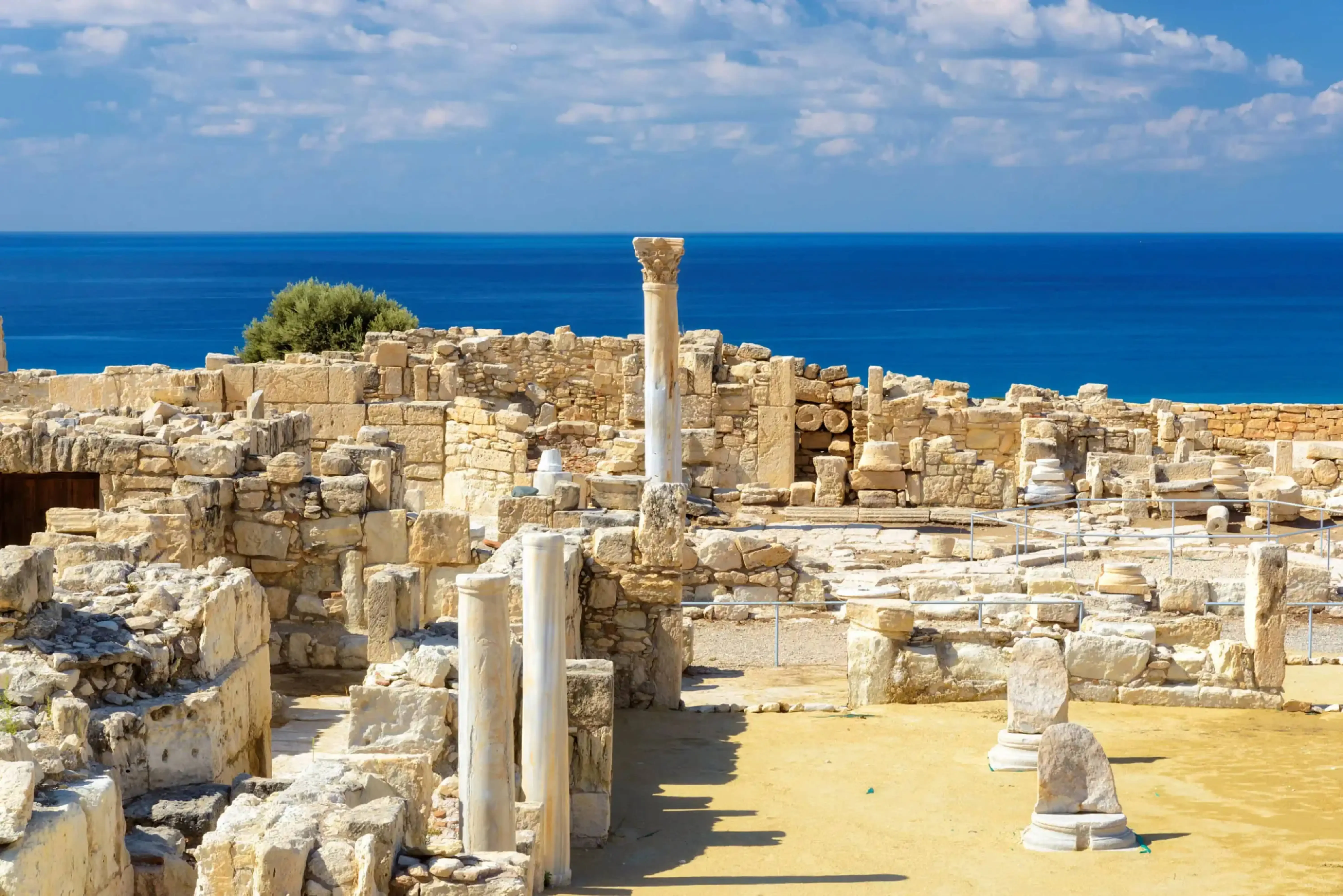 Ancient stone ruins of a Greco-Roman site overlooking the Mediterranean Sea under a partly cloudy sky.