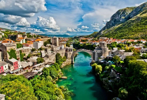 Aerial view of the historic Stari Most (Old Bridge) spanning the emerald green Neretva River, surrounded by traditional stone buildings and lush greenery in Mostar, Bosnia and Herzegovina.