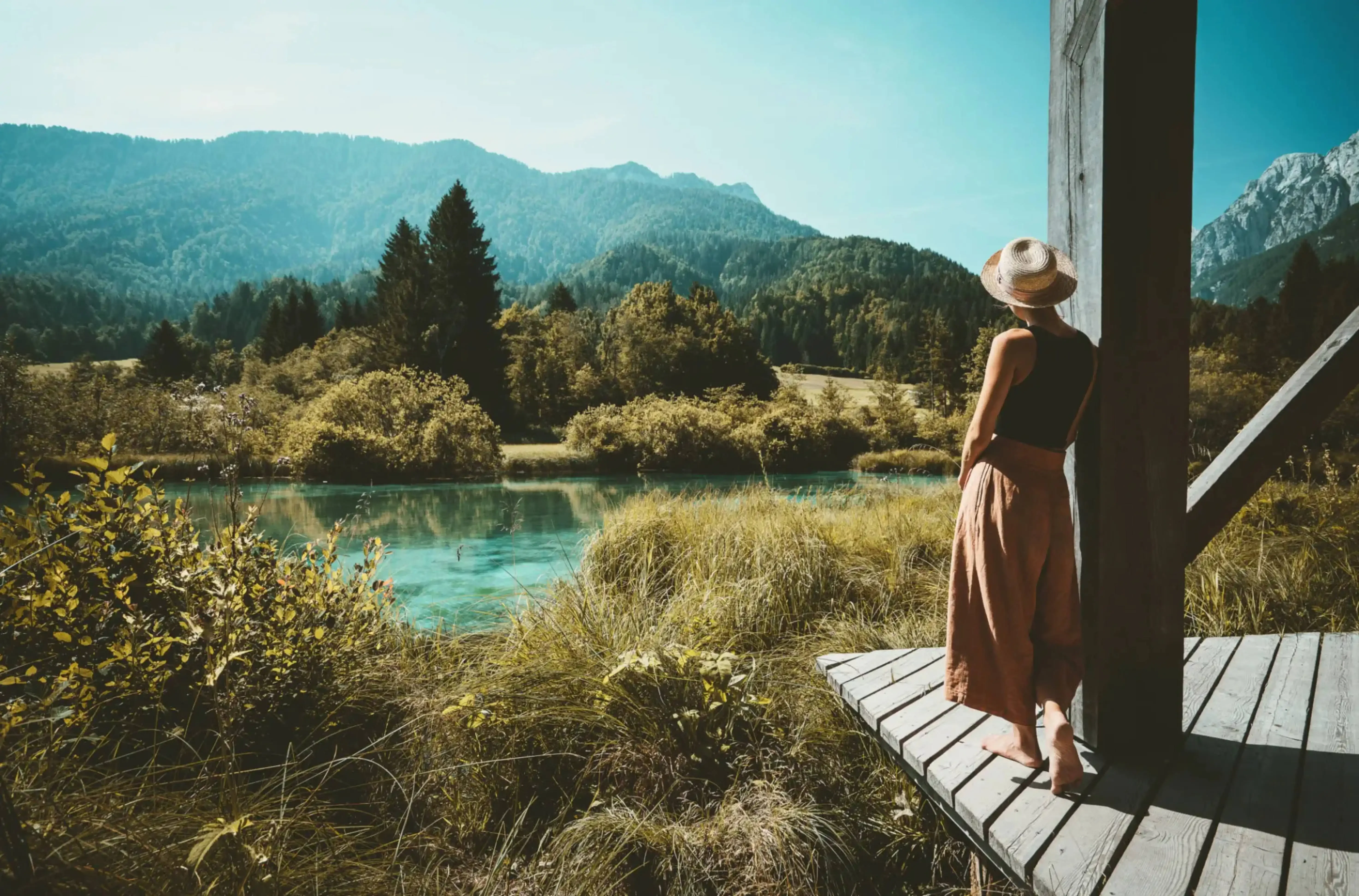 Solo female traveler enjoying scenic mountain view from a wooden platform overlooking a turquoise river in a peaceful nature retreat