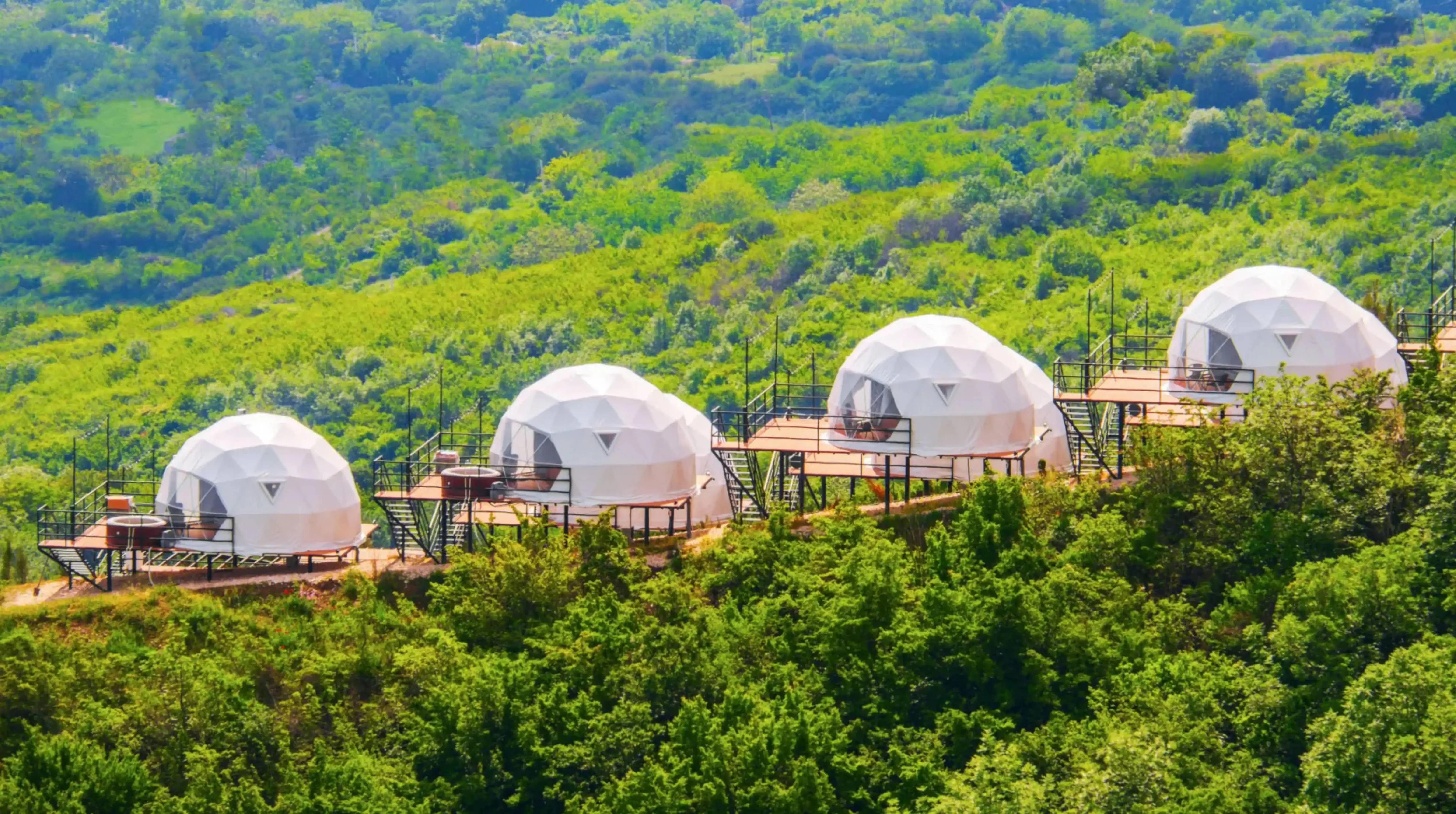 Eco-friendly glamping domes nestled in a lush green forested hillside, ideal for luxury nature retreats