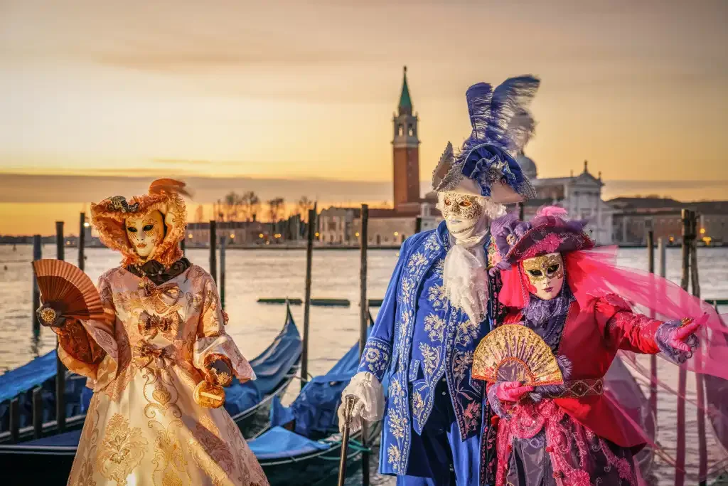 People in ornate Venetian carnival costumes and masks posing by the Grand Canal in Venice at sunset