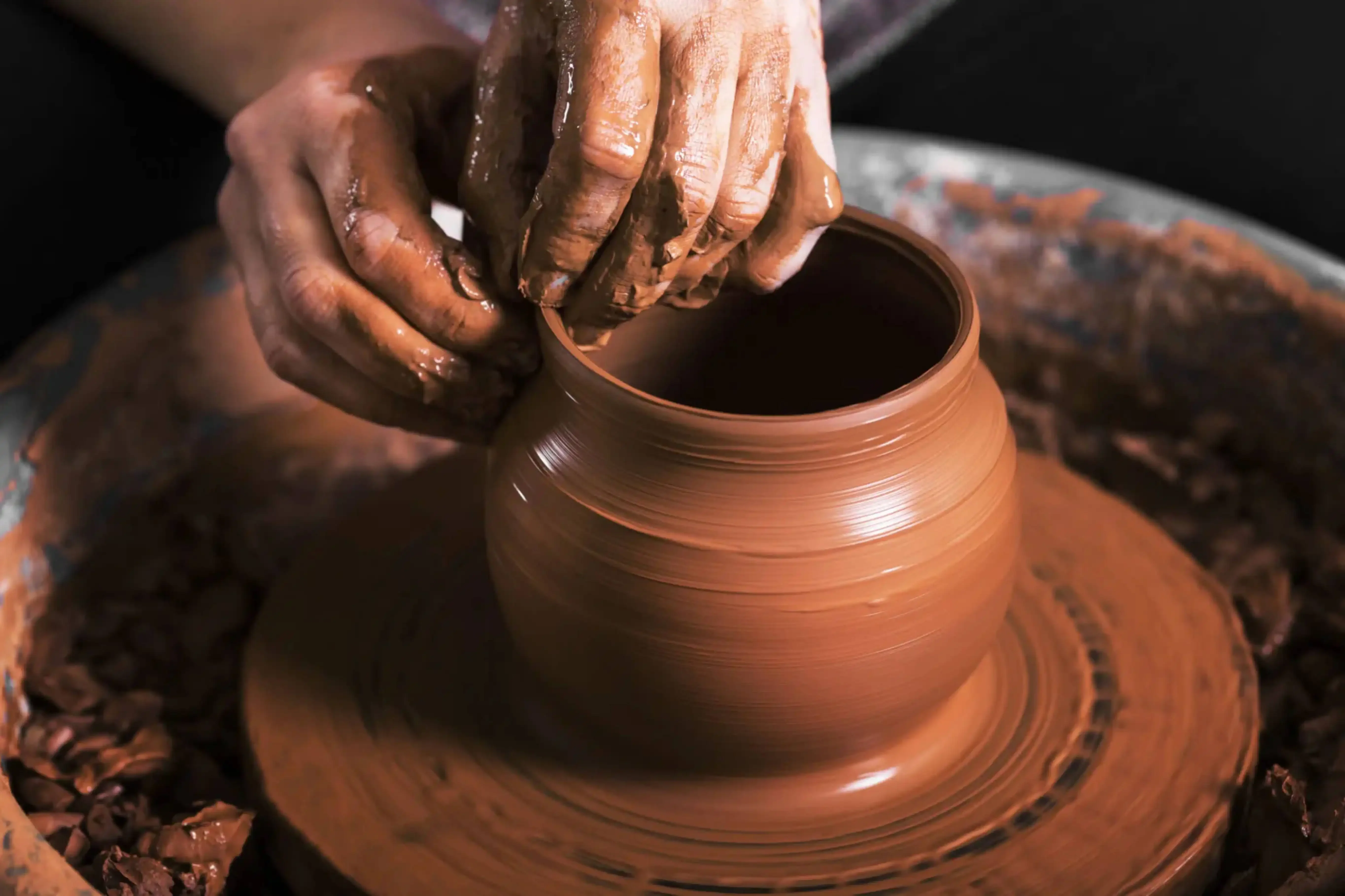 Close-up of hands shaping a clay pot on a traditional pottery wheel during a cultural craft workshop