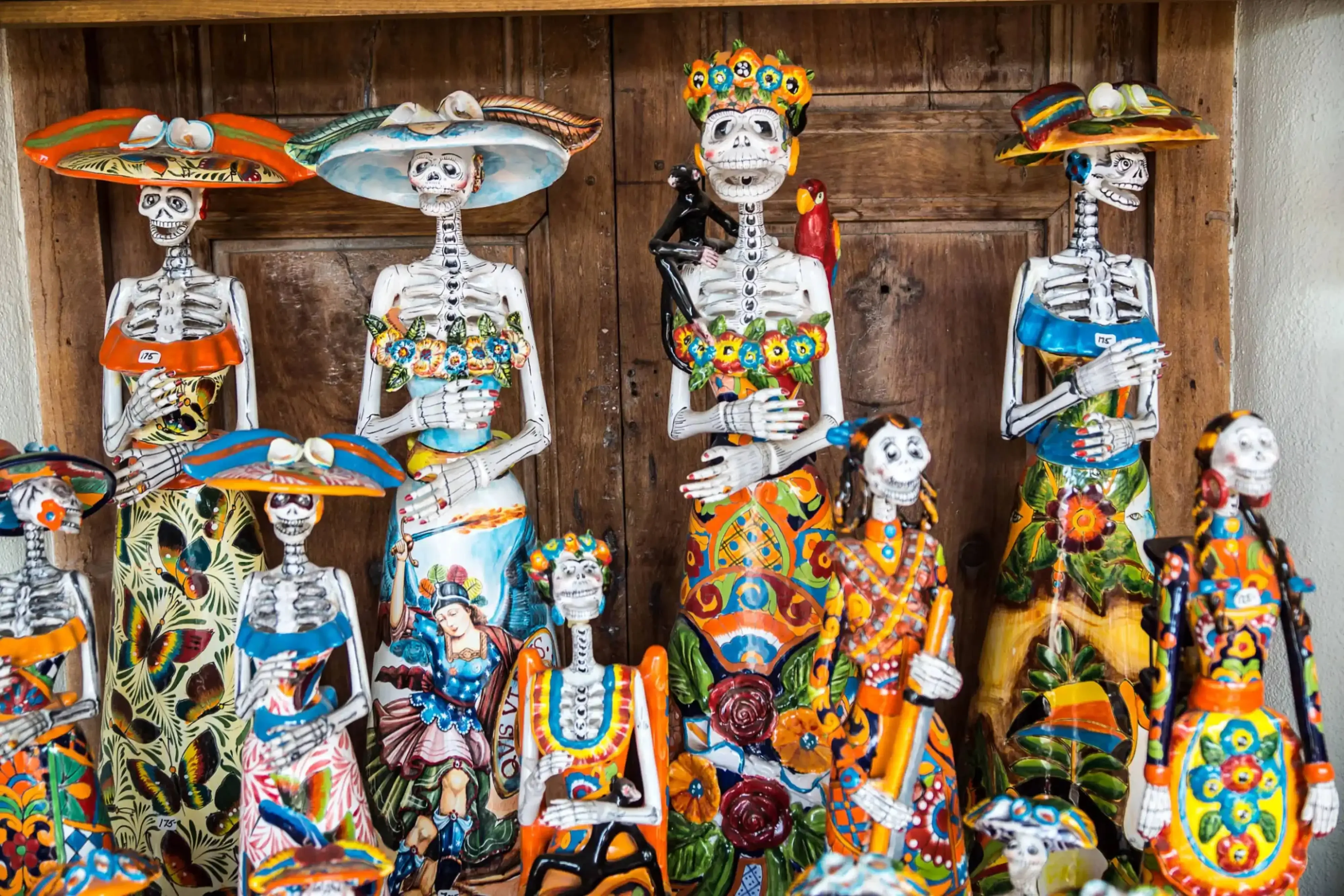 Colorful Day of the Dead ceramic skeleton figures in traditional Mexican attire displayed against a wooden backdrop