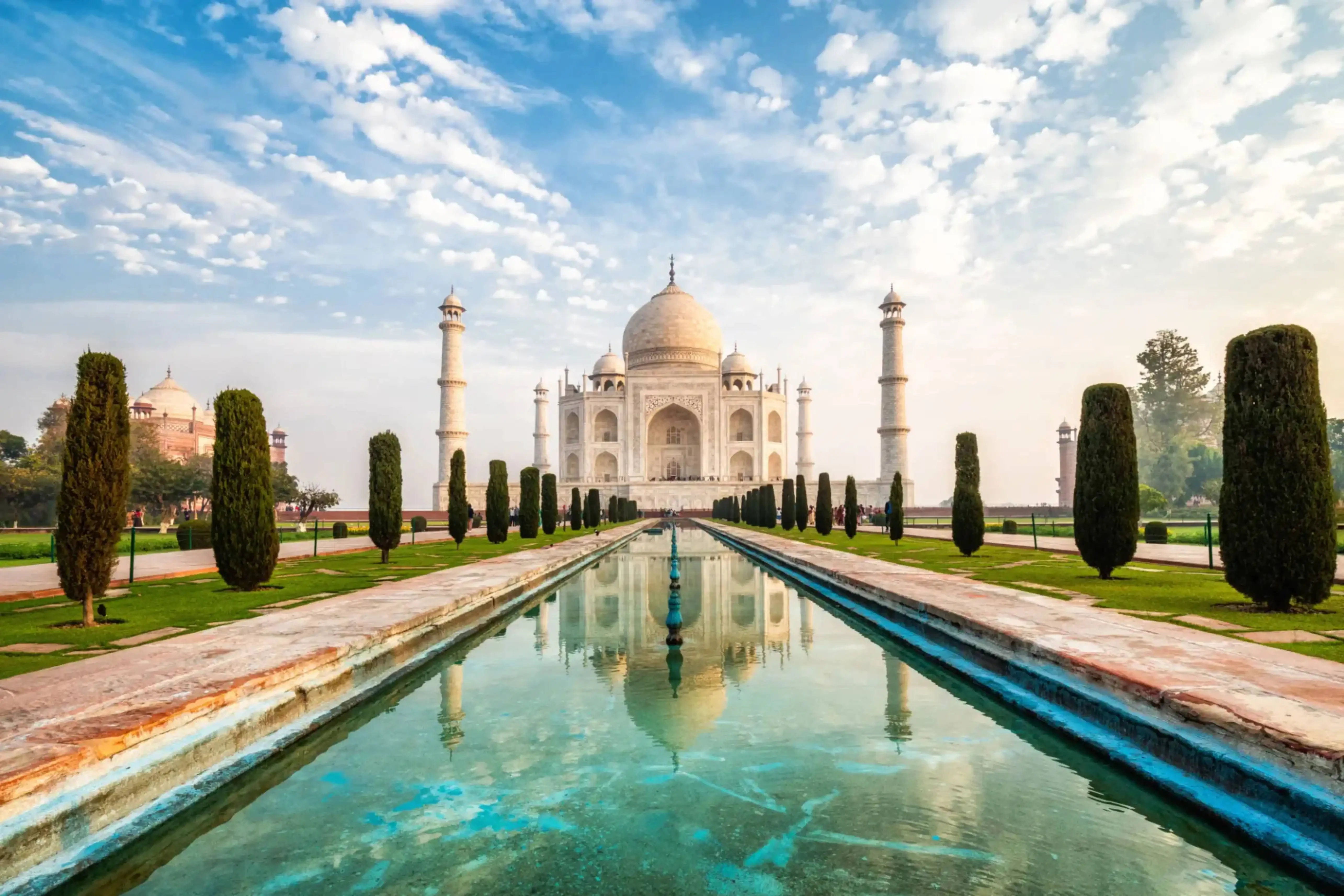 Symmetrical view of the Taj Mahal with its reflection in the long water channel under a blue sky, located in Agra, India