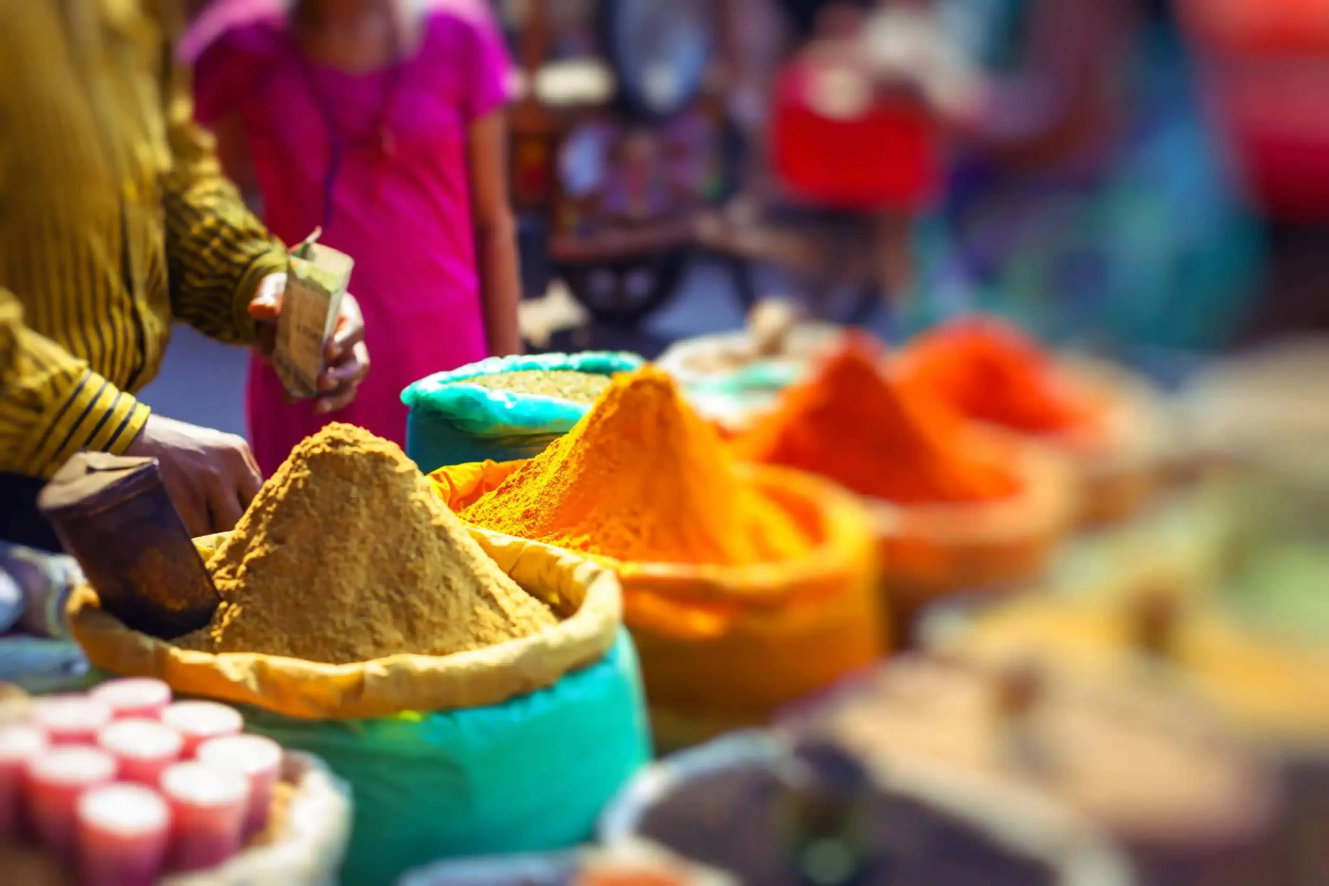 Colorful spices on display in open sacks at a vibrant Indian street market, with people shopping in the background