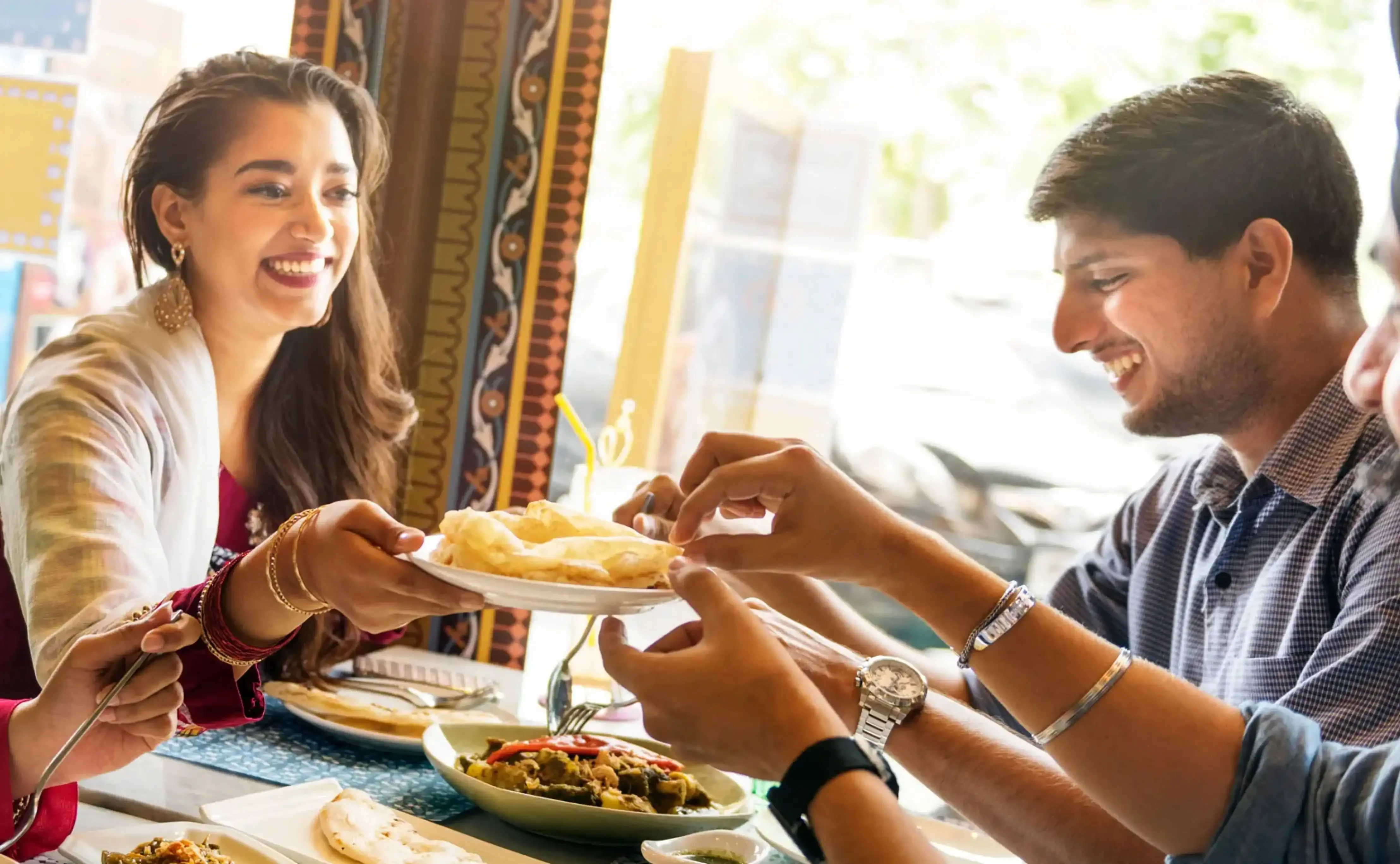 Group of smiling friends sharing traditional Indian food at a restaurant table