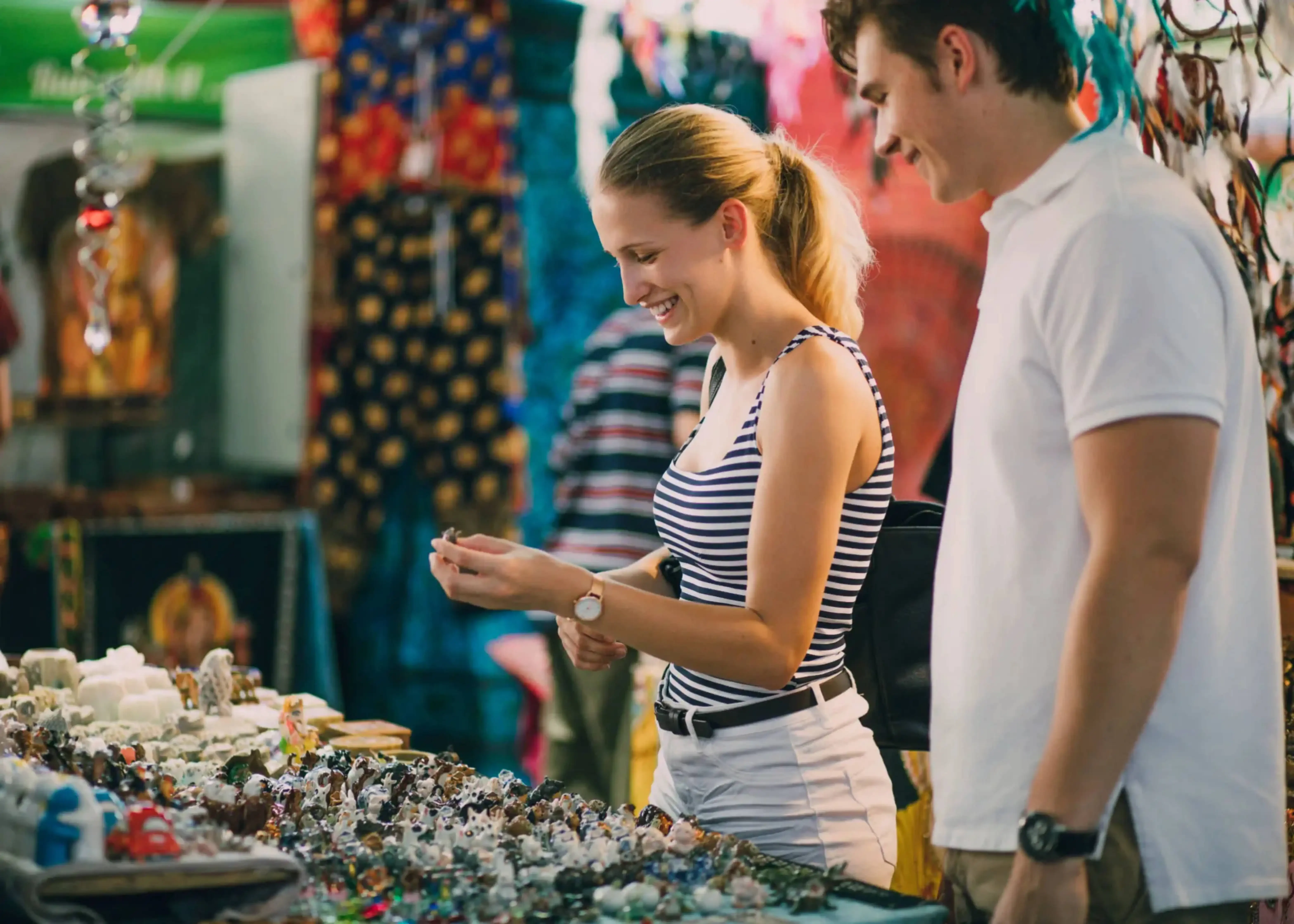 Smiling couple shopping at a colorful street market, browsing handmade jewelry and local souvenirs