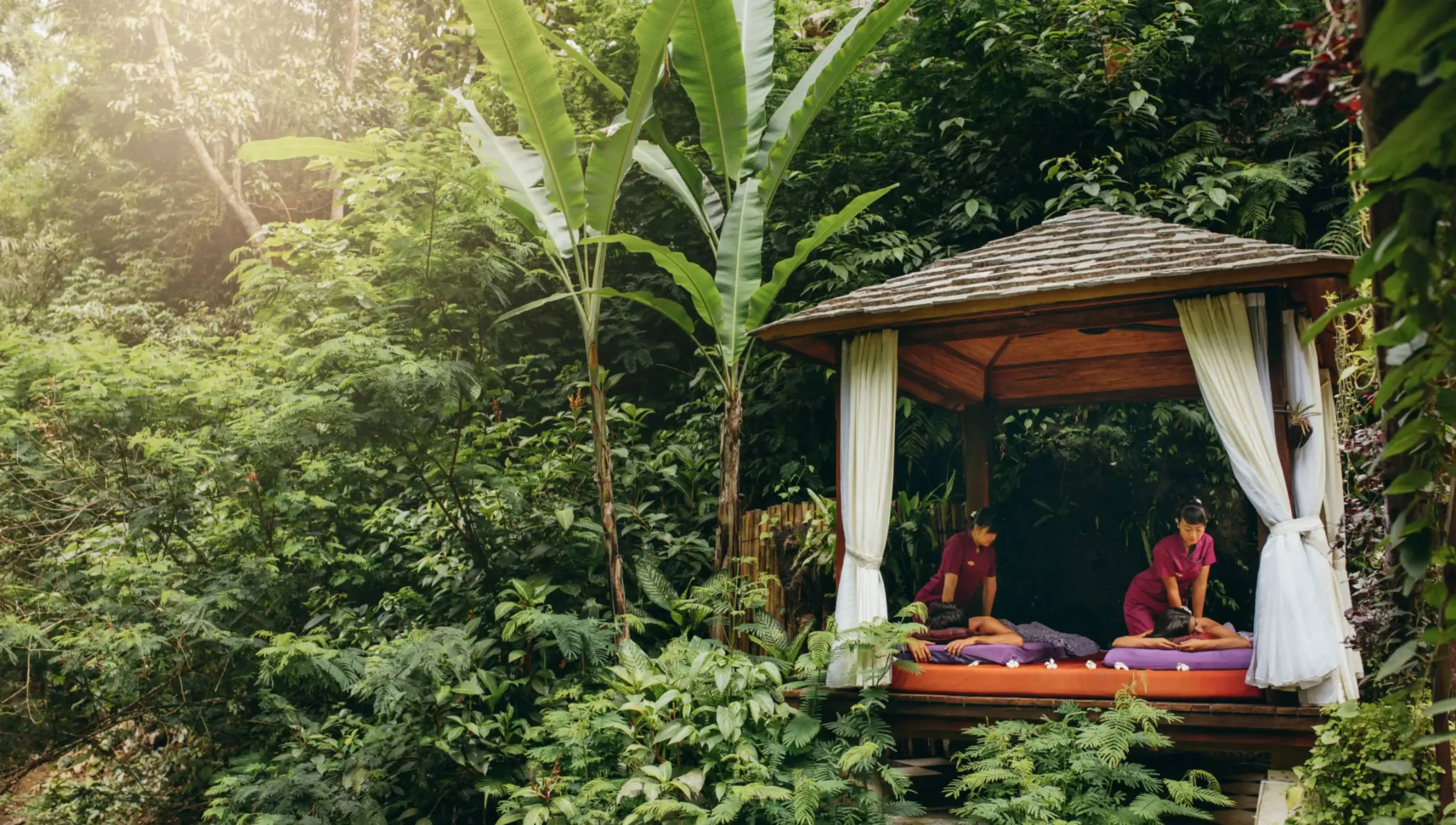 Outdoor spa pavilion with massage therapists providing treatments in a lush tropical jungle setting