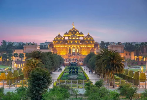 Sunset view of Akshardham Temple in Delhi, India, illuminated with golden lights and surrounded by lush gardens