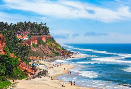 Scenic view of Varkala Beach with red cliffs, palm trees, and ocean waves in Kerala, India