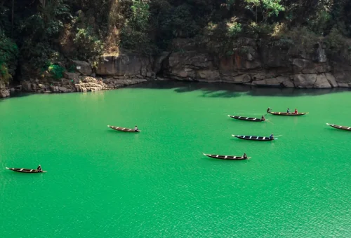 "Traditional wooden boats floating on the emerald-green waters of Dawki River, Meghalaya, with forested cliffs in the background"