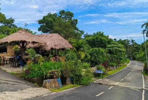 "Traditional Khasi thatched-roof house and landscaped garden at a road junction in Meghalaya village, India"