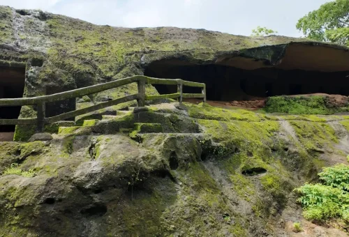"Moss-covered ancient rock formation with railing and steps at Arwah Cave entrance in Meghalaya"