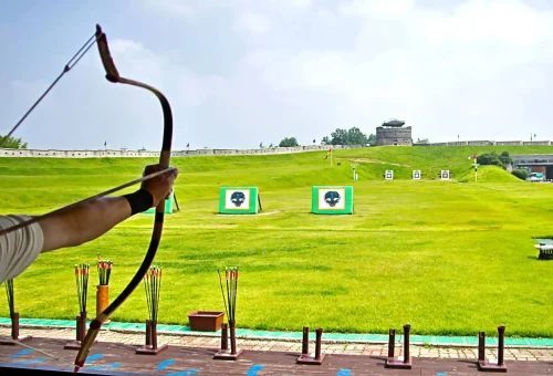 "Person aiming a bow and arrow at archery targets on a grassy field in Meghalaya, India"