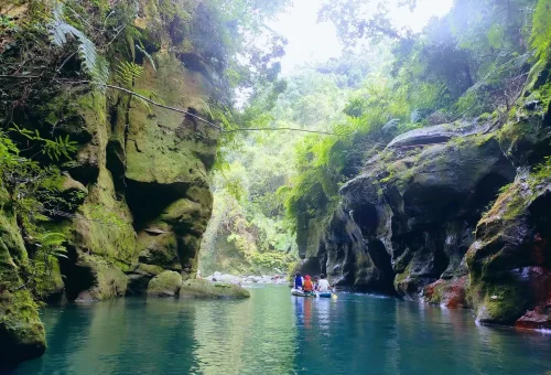 Wari-chora- "People kayaking through a narrow emerald canyon surrounded by rocky cliffs and lush greenery"