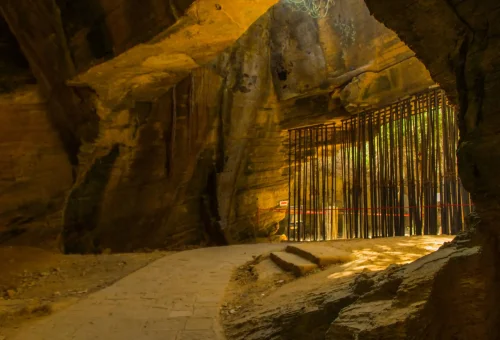 "Sunlight filtering through a narrow bamboo fence inside a dimly lit cave passage"