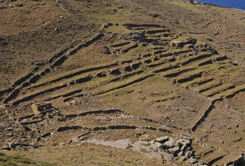 "Ancient stone ruins and terraced formations on a dry, hilly landscape under clear daylight"
