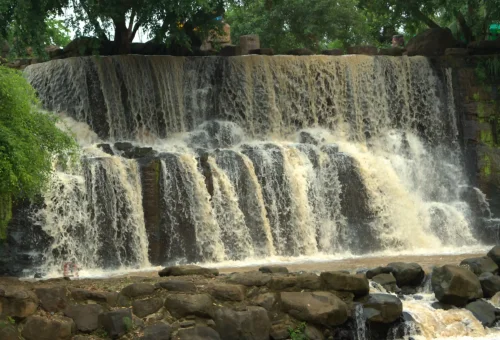 "Multi-tiered cascading waterfall surrounded by lush greenery and flowing over rocky steps"