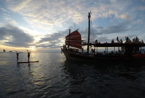 Traditional red sail boat and guests paddleboarding during a Krabi sunset cruise