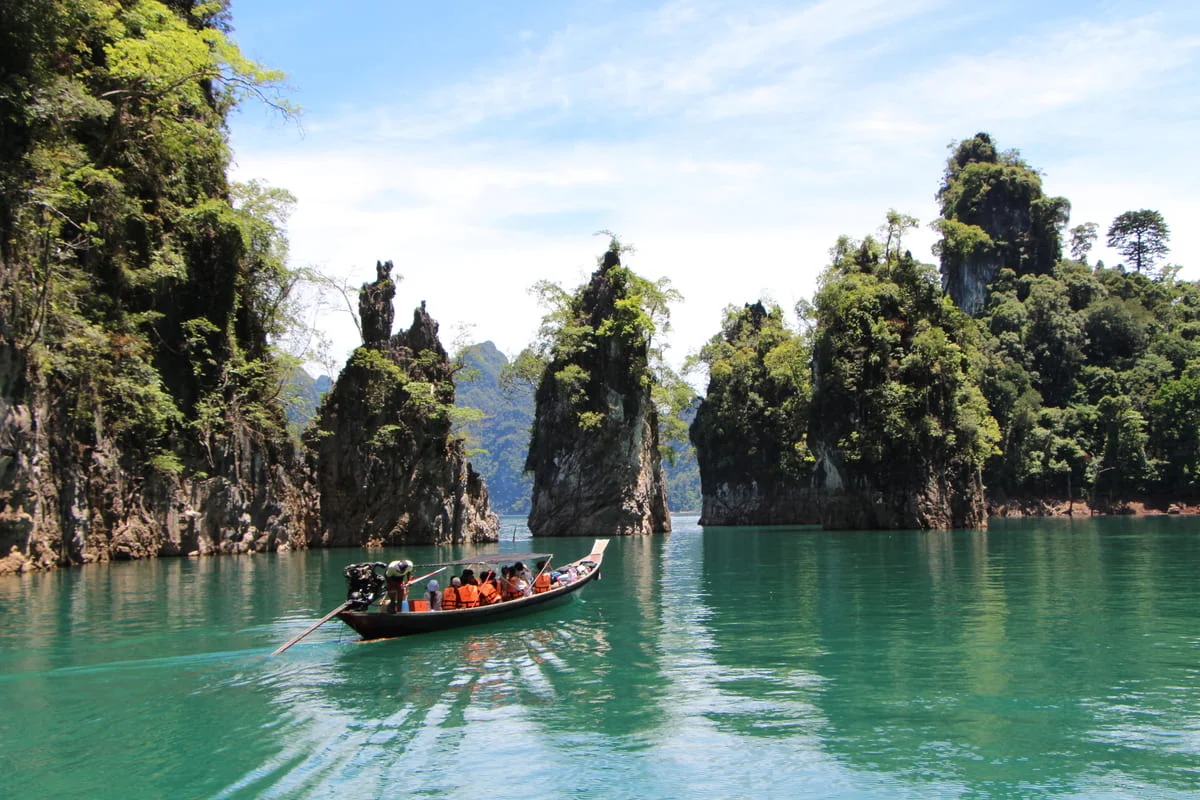 Traditional longtail boat travelling between towering limestone cliffs on Cheow Lan Lake