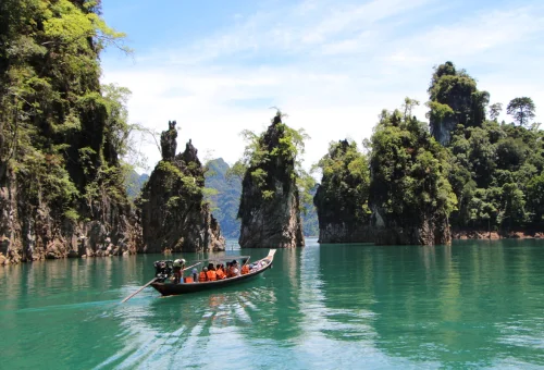 Traditional longtail boat travelling between towering limestone cliffs on Cheow Lan Lake