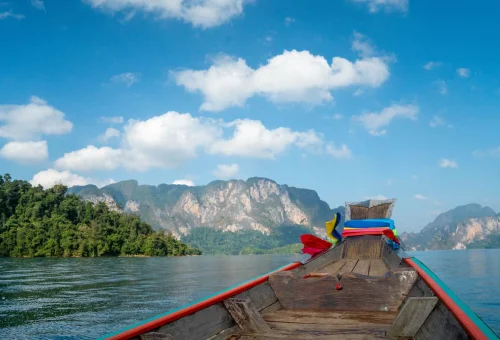 View from a traditional longtail boat cruising across Cheow Lan Lake with limestone cliffs and green mountains in the distance
