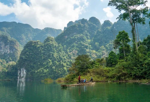 Traditional bamboo raft carrying visitors across the calm waters of Cheow Lan Lake surrounded by rainforest and limestone cliffs