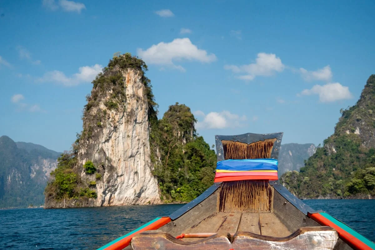 Traditional Thai longtail boat cruising past dramatic limestone mountains on Cheow Lan Lake in Khao Sok National Park