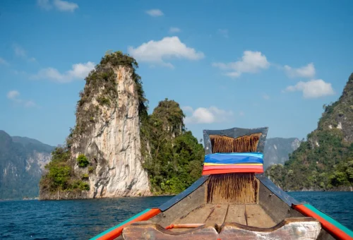 Traditional Thai longtail boat cruising past dramatic limestone mountains on Cheow Lan Lake in Khao Sok National Park