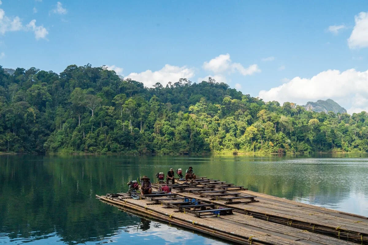 Traditional bamboo raft floating across Cheow Lan Lake surrounded by green rainforest and scenic mountain views