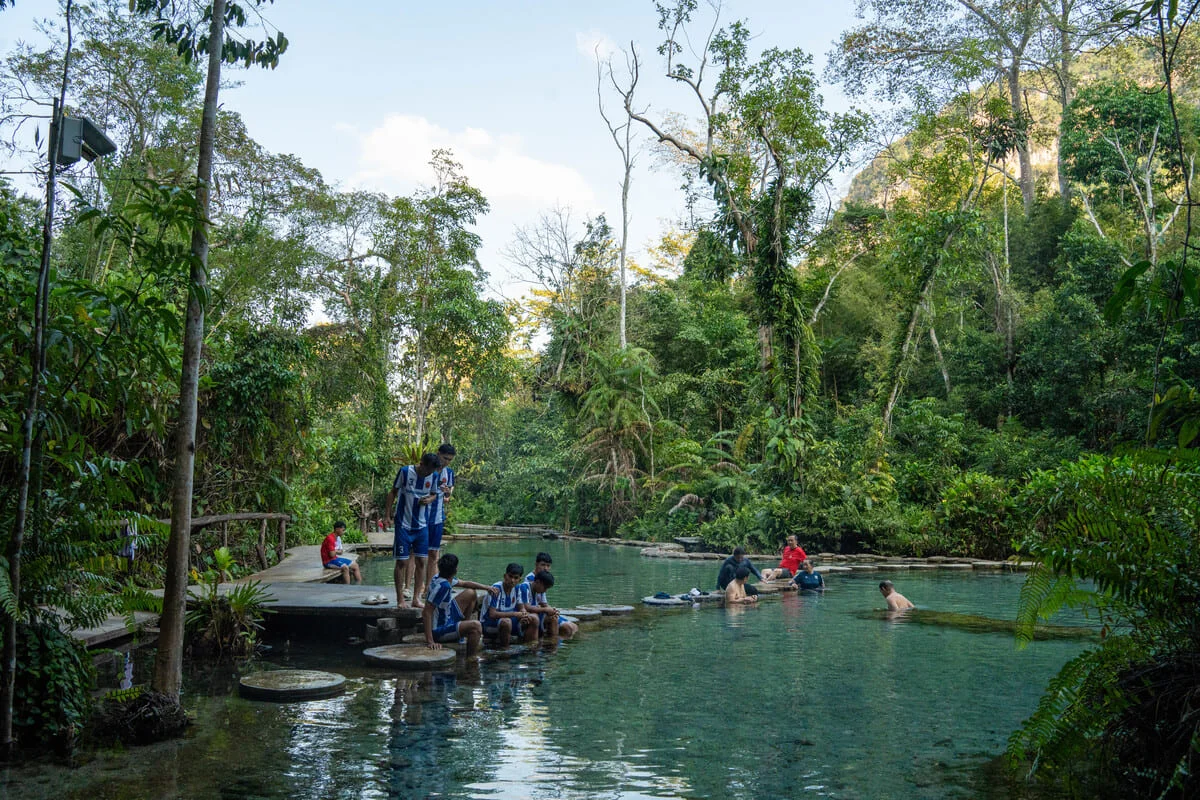 Visitors relaxing beside a clear natural pool surrounded by tropical rainforest in southern Thailand