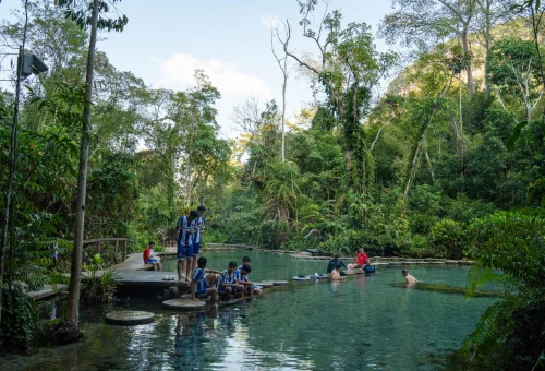 Visitors relaxing beside a clear natural pool surrounded by tropical rainforest in southern Thailand