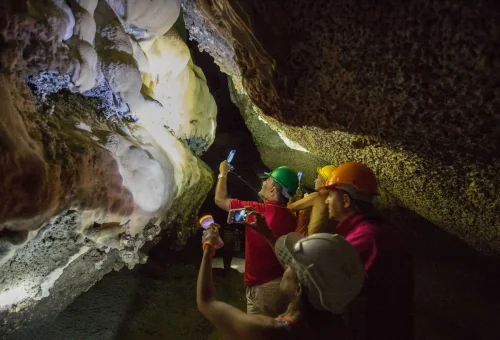Adventurers hiking through a dramatic limestone cave with sunlight filtering through the entrance, during the early departure James Bond Island Tour.