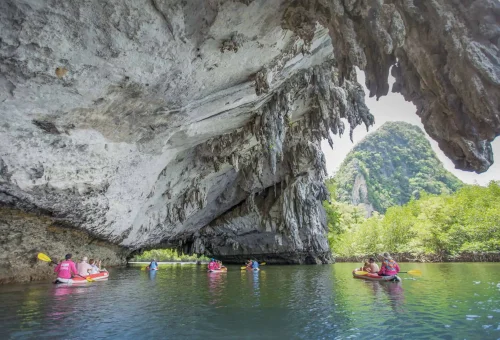 Guests canoeing through a narrow sea cave surrounded by towering limestone walls and calm emerald waters during the early departure James Bond Island Tour.