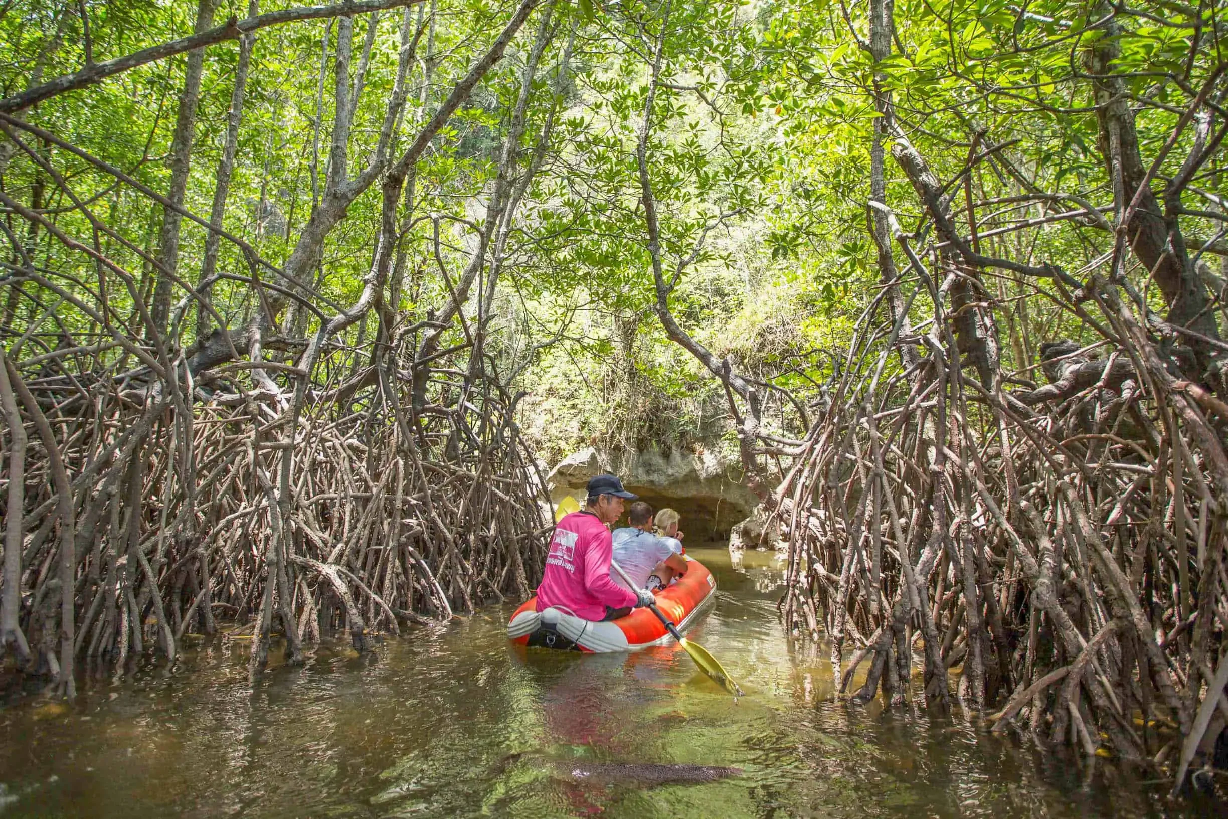 Guests paddling through sea caves and limestone cliffs in a canoe during the early departure James Bond Island Tour, surrounded by calm emerald waters.