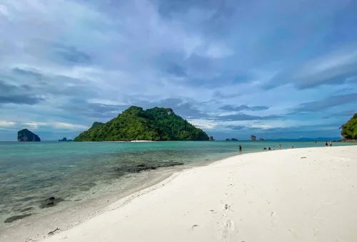 Beautiful scene of Poda Island on the Krabi 4 Islands tour — white sandy beach, turquoise sea, and a towering limestone rock just offshore.