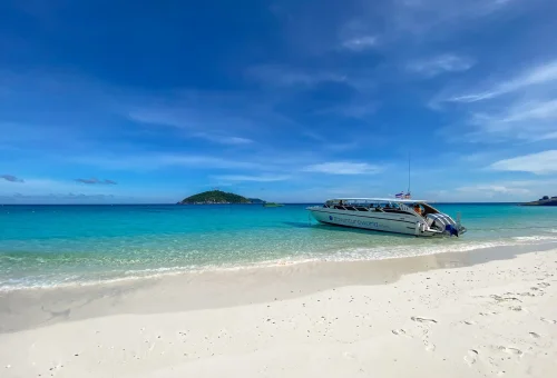 A speedboat floating in the turquoise waters of Princess Bay, Similan Islands, surrounded by white sand beach and tropical forest.
