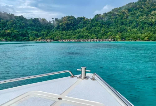 Boat approaching the Moken Village at Surin Island with traditional stilt houses lining the shore and lush jungle in the background