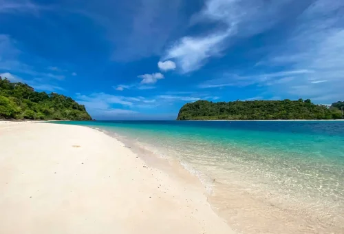 Pristine white sand beach at Koh Rok with clear turquoise water and lush tropical backdrop under sunny skies