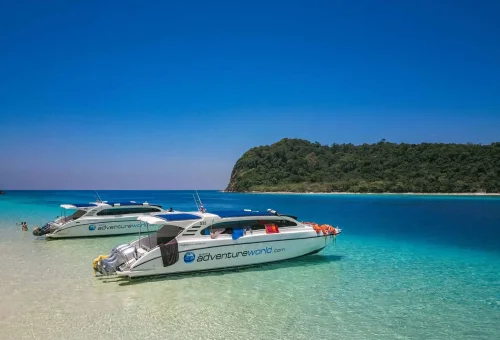 Vibrant beach scene at Koh Rok with clear turquoise water, white sand, and excited tourists enjoying the tropical atmosphere