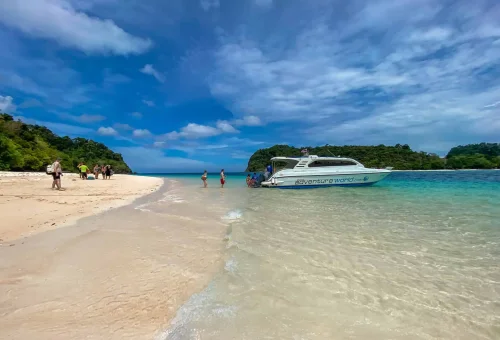 Tourist stepping off a boat onto the white sandy beach of Koh Rok with clear turquoise water and tropical surroundings