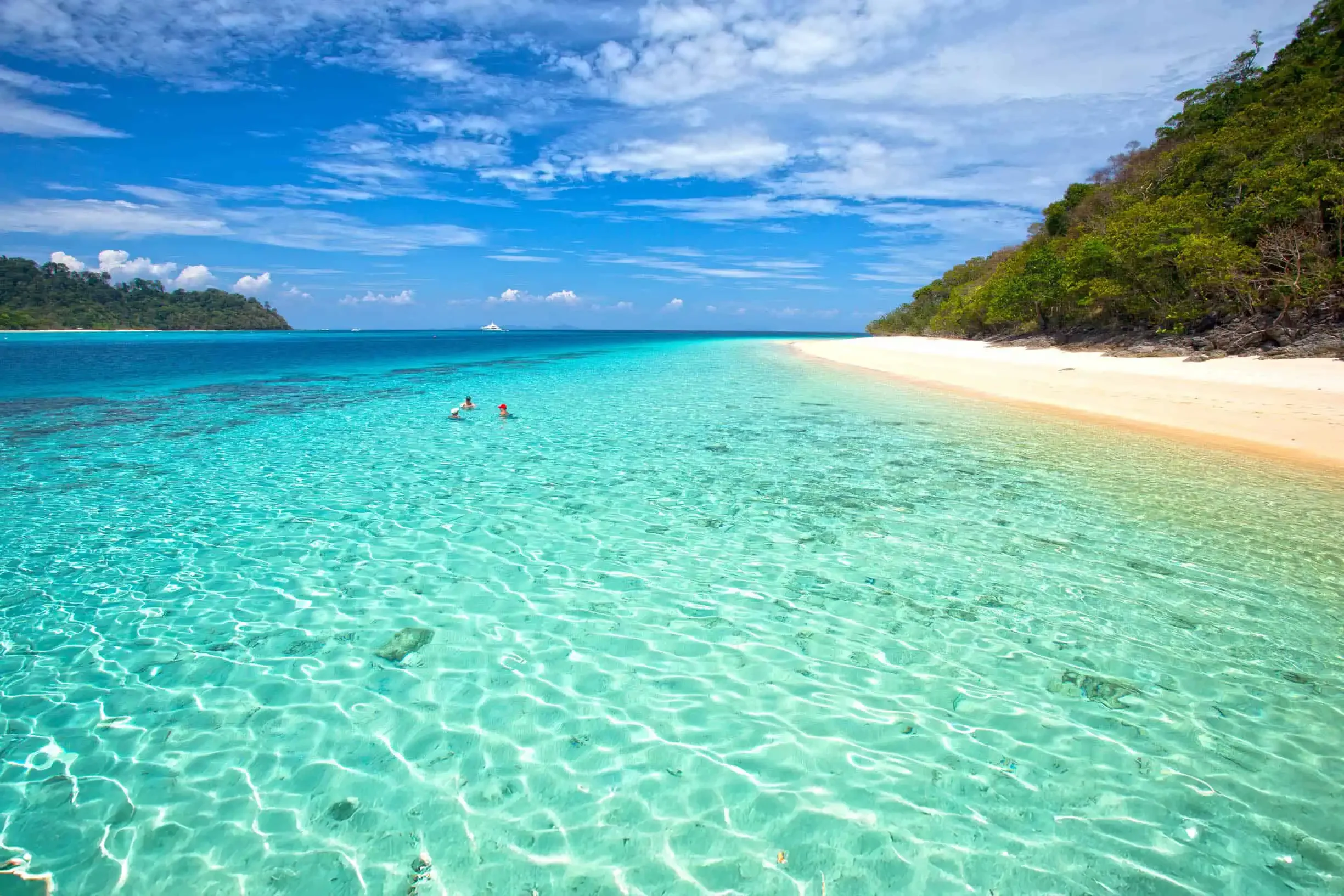 Tourist swimming in the crystal-clear turquoise waters of Koh Rok with white sandy beach and tropical backdrop