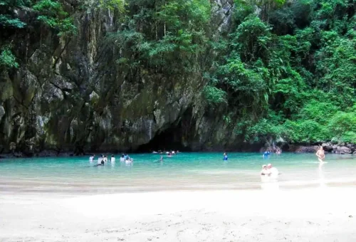 Tourists swimming through the dark entrance of the Emerald Cave at Koh Mook, surrounded by limestone cliffs and turquoise water